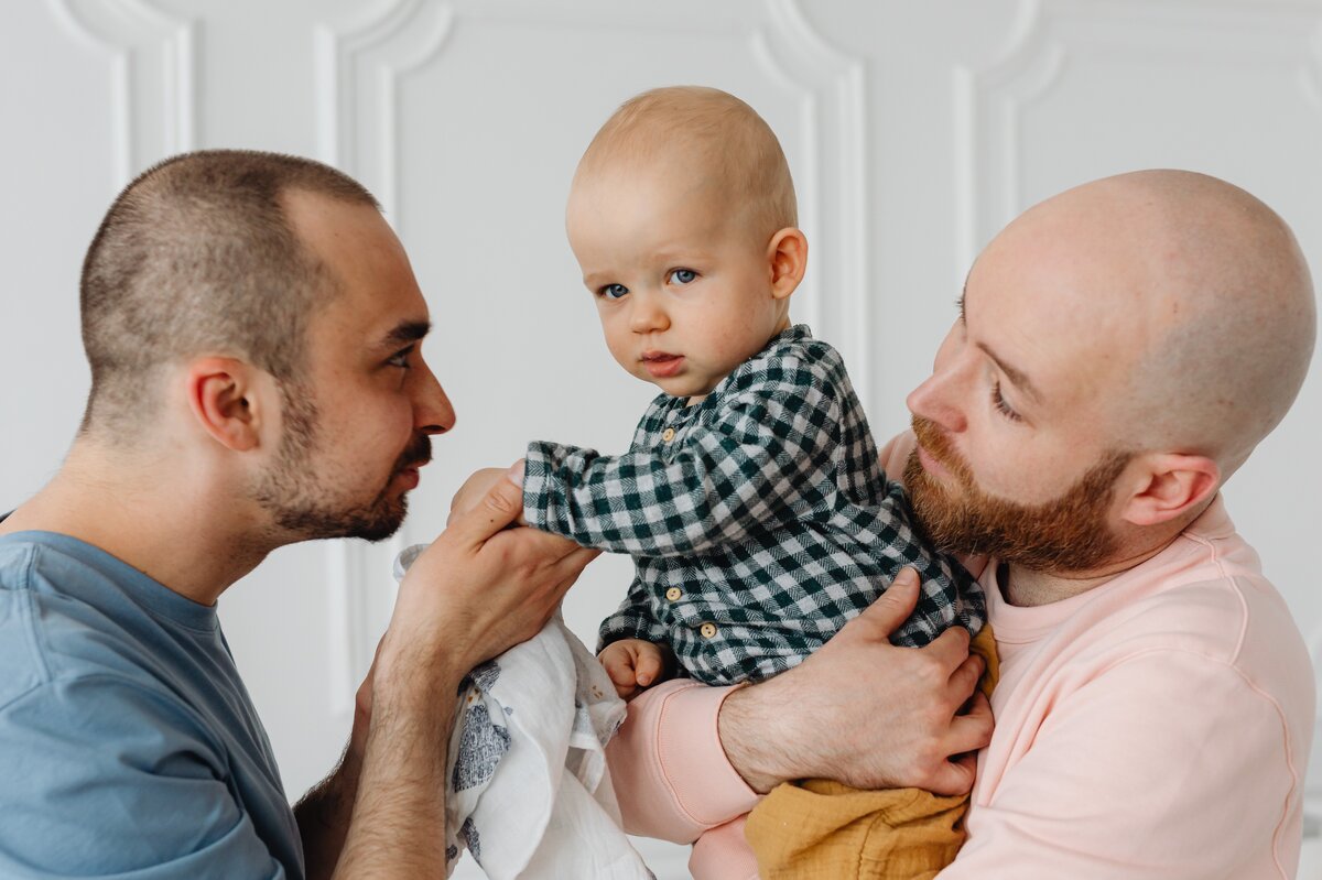 Image shows two men holding a baby