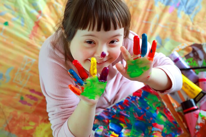 Image shows a child with paint-covered hands smiling at the camera